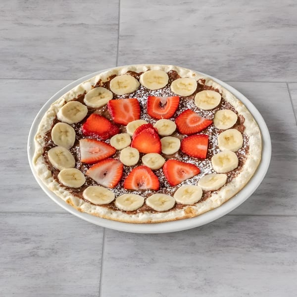 A dessert pizza with Nutella, sliced strawberries, and bananas, dusted with powdered sugar.