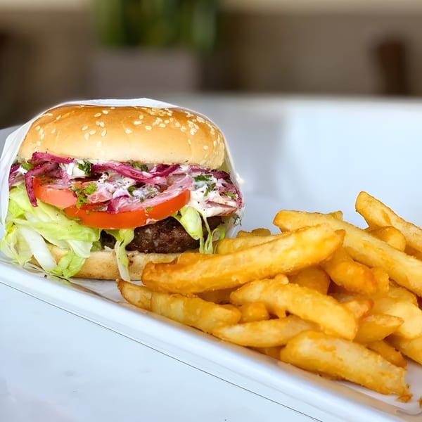 A Tarme Mediterranean Grill burger with lettuce, tomato, red onion, and sauce, served with fries.