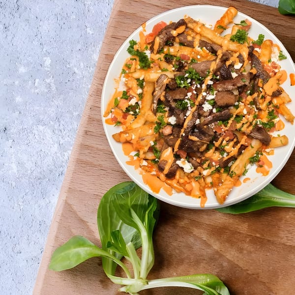 Tarme Mediterranean Grill's loaded fries with meat, sauce, feta, and parsley on a white plate.