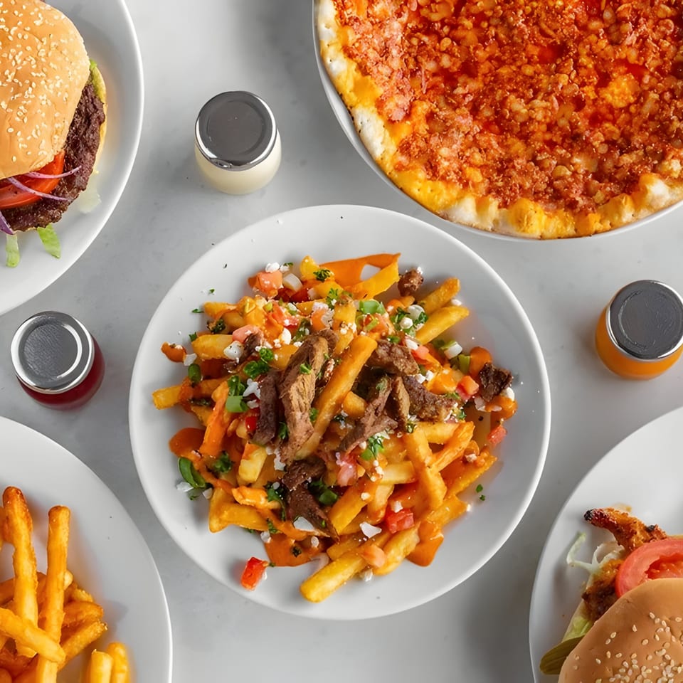 Overhead view of Tarme Mediterranean Grill's loaded fries, pizzas, and burgers on a white table.