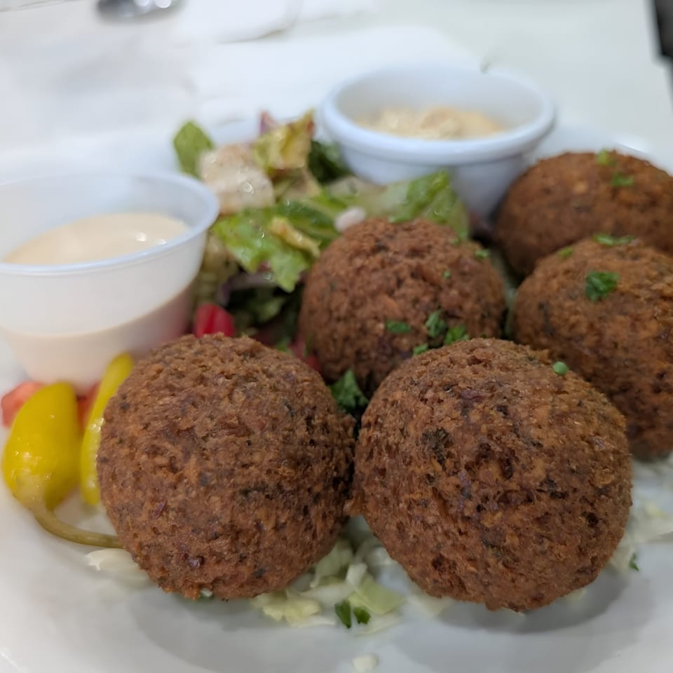 A plate of Tarme Mediterranean Grill falafel, salad, and two dipping sauces.